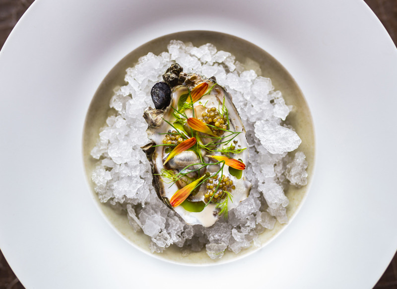 An oyster, bedded in crushed ice and filled with caviar, fennel herb and chamomile, finds its perfect backdrop on the brass-colo